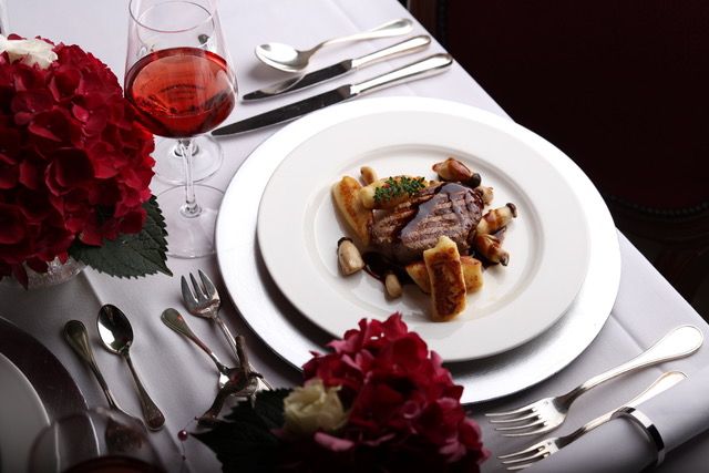 Festlich angerichteter Hauptgang mit Rinderfilet und Gnocchi, daneben Rotwein und rote Hortensien