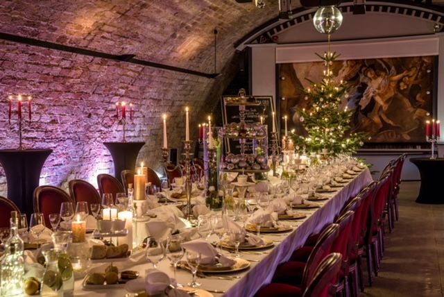 Weihnachtlich gedeckte lange Tafel mit Kerzen und Weihnachtsbaum im Gewölbesaal
