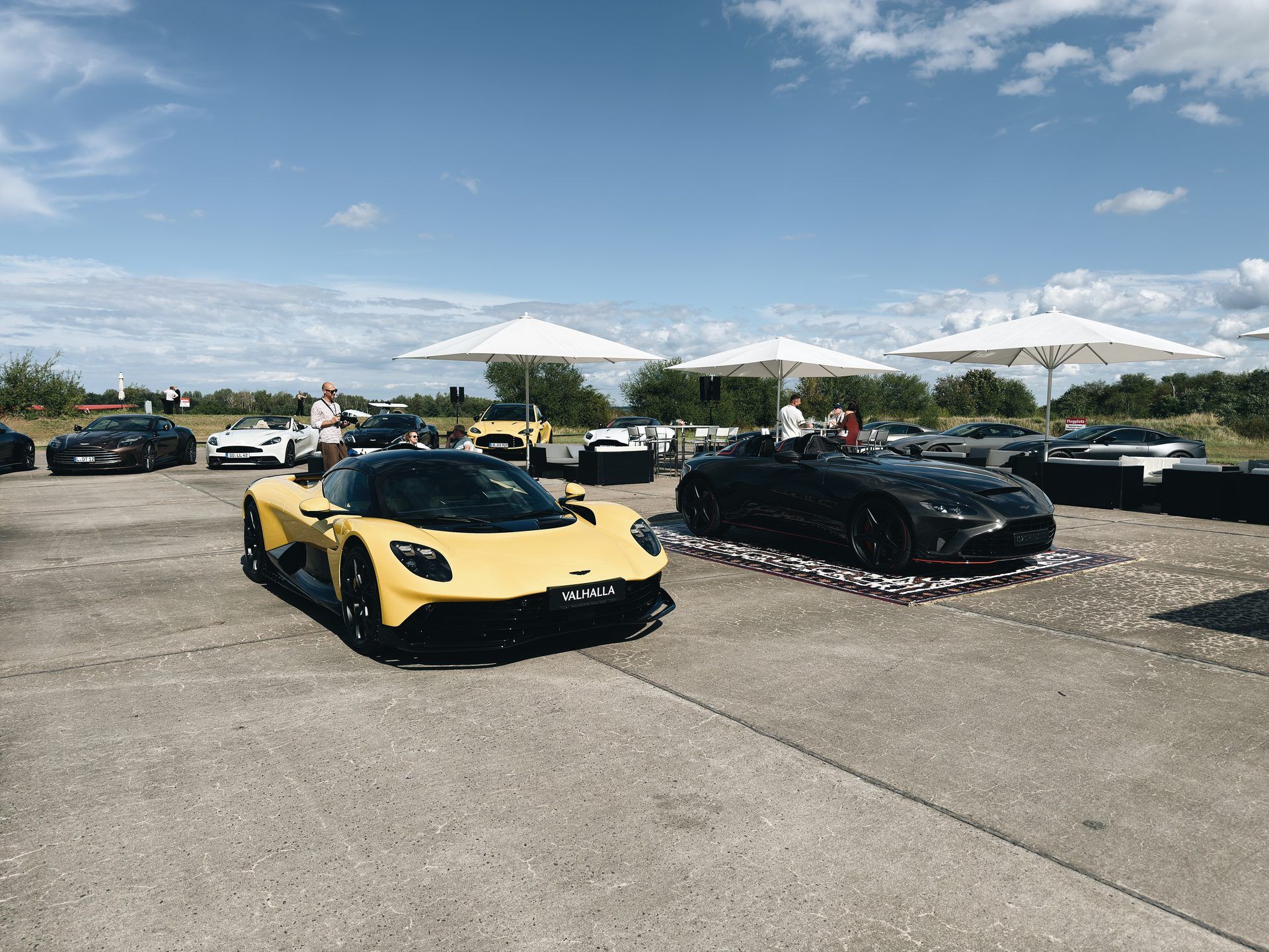 Gelber Aston Martin Valhalla und weitere Sportwagen auf dem Vorfeld des Flugplatzes Großenhain